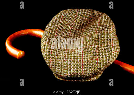 Tweed cap and walking stick isolated on a black background