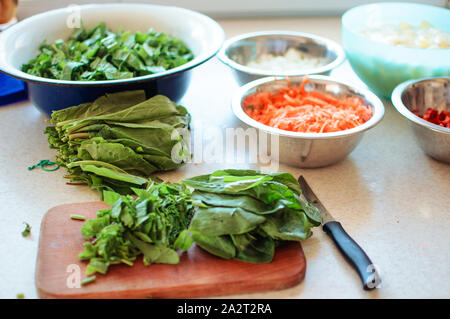 Bright fresh leaves of sorrel on a cutting board. Rustic style, against the background of vegetables in bowls: carrots, onions, pepper chopped.Copy sp Stock Photo