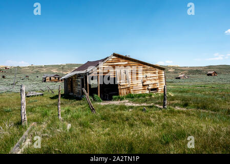 Old abandoned wooden barn with fence posts, surrounded by green grass and sage brush at Bodie State Historic Park in the eastern Sierra. Stock Photo