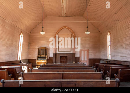 Inside the old Methodist church at Bodie State Historic Park, in California, with rows of pews and small church organ (centered). Stock Photo