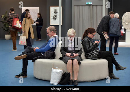 Members of the public, art lovers and collectors talk on their mobile phones and check their messages as they attend the opening day of the art fair F Stock Photo