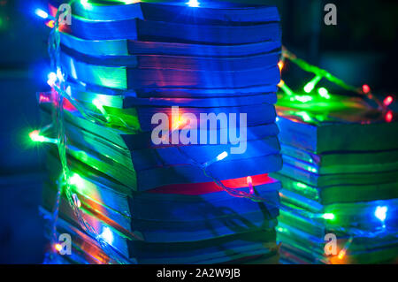 Christmas light coiled all around on a tower of books. String lights. Close up shot of book compilations. Blue wallpaper. Stock Photo