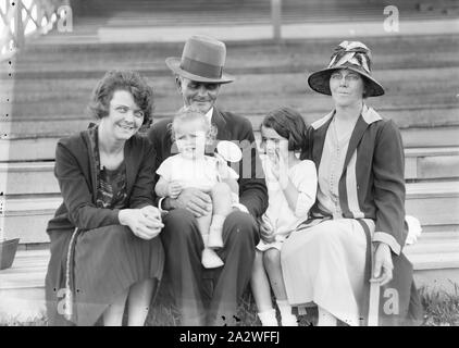 Glass Negative - Family Portrait in Stadium, circa 1930s, A black and white, half plate negative featuring a family seated in a grandstand. The group is made up of two women, a man in a tall hat, and two children (a baby and young girl Stock Photo