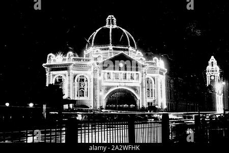 Negative - Melbourne, Victoria, 1920, Flinders Street Railway Station illuminated for the Prince of Wales visit. The photograph has been taken from the front of St Paul's Cathedral across the wet intersection of Flinders and Swanston Sts Stock Photo