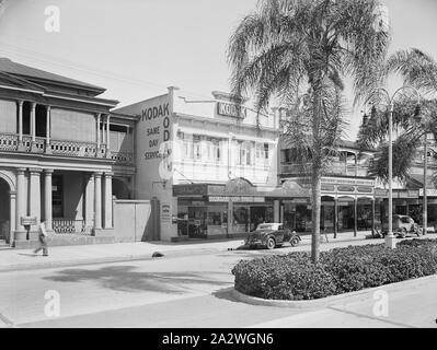 Negative, Shop Exterior Kodak Branch, Townsville, QLD, 1930s, Black and white film negative of the Kodak Australasia Pty Ltd branch store and same day processing laboratory on Flinders St, Townsville, Queensland, in the 1930s. This street view shows neighbouring shops, a vegetated traffic island, and cars and bicycle parked on the street out front. A man is walking out the front of the Queensland National bank to the left of the shot. This Kodak store was Stock Photo