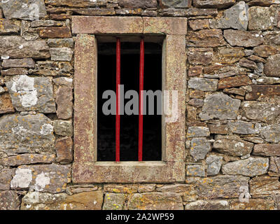 2 vertical red iron bars across sandstone bordered window of stone barn with cracked lintel on a farm in Cumbria,England,UK Stock Photo