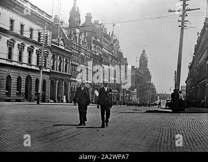 Negative - Melbourne, Victoria, circa 1900, Collins street, looking west. Two men, both wearing straw boaters, are crossing the street in the foreground. The tower of the Federal Hotel is visible in the background Stock Photo