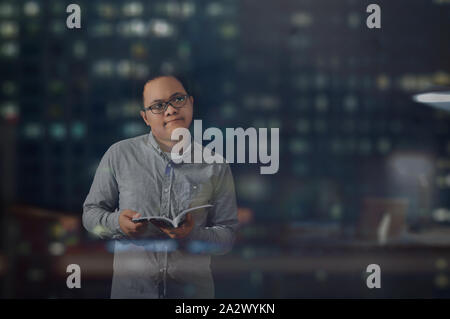 Young business man temporarily looking at something else and thinking and analyzing an idea while reading and holding a book inside an office room. Stock Photo