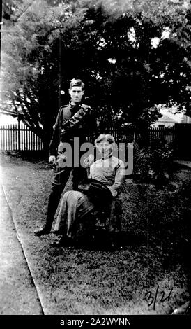 Negative - Victoria (?), circa 1915, A woman seated in a garden with a boy standing beside her. The boy is wearing military (cadet?) Uniform and a bandolier. The woman is holding a slouch hat Stock Photo