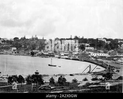 Negative - Woolloomooloo Bay or Rushcutters Bay(?), Sydney, New South Wales, circa 1870s, View overlooking a cove on Sydney Harbour, possibly Woolloomooloo Bay or Rushcutters Bay. There is a lone yacht, small single-masted trading vessel like a cutter anchored in the bay with a small dingy moored to its stern. Two other small sailing vessels are moored near the wharves in the background. Some form of land reclaimation work appears to be underway near the foreshore with piles of rock Stock Photo