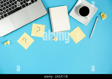 Asking, Decisions. Question mark on sticky notes, notebook, cup coffee, laptop and pen on blue background. FAQ concept. Working with clients. Troubles Stock Photo