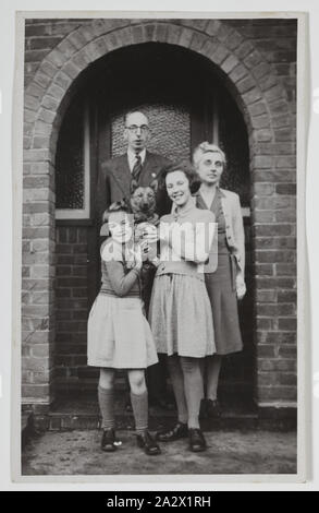 Photograph - Palmer Family Outside House, Iver, England, circa 1947, Black and white photograph of George and Gertrude Palmer and their daughters Shirley and Lesley, and their dog Robbie, in England around 1947. It was probably taken at George's sister's house in Iver, Buckinghamshire by George's brother-in-law David Roberts, the day before they left for Australia. It was brought to Australia by George Palmer when he migrated to Australia from England with his wife Stock Photo