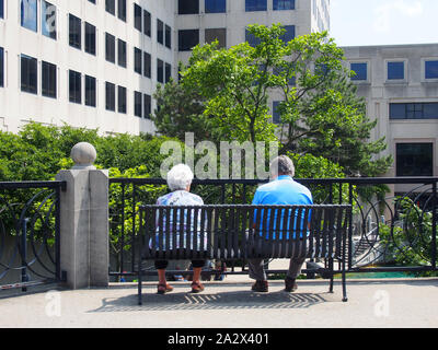 Senior couple sitting on bench in city park overlooking Indianapolis Canal Walk, Indianapolis, Indiana, USA, July 27, 2019, © Katharine Andriotis Stock Photo