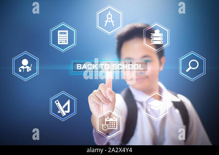 School boy wearing in school uniform and back pack bag pressing the button Back to school using hologram on isolated blue background Stock Photo