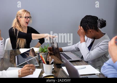 Furious Businesswoman Shouting At Female Employee Working On Laptop At Workplace Stock Photo