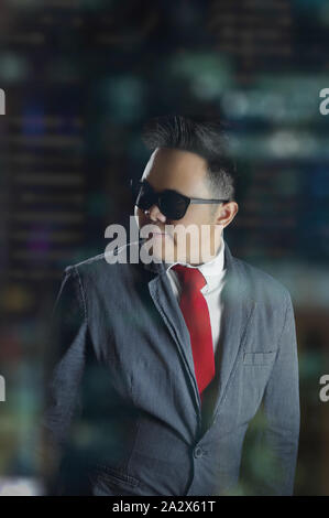Portrait of young business man in corporate attire looking over the shoulder and smiling with an open mouth. A night shot portrait inside an office. Stock Photo