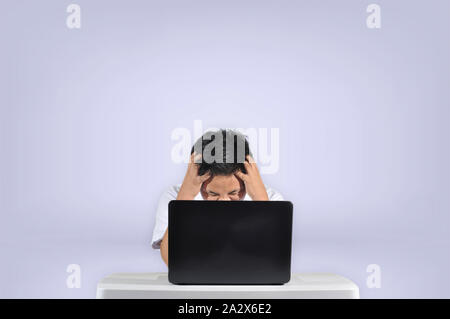 Young male student getting angry in front of his laptop frustrated while doing his project or assignment concept in a white isolated background. Stock Photo