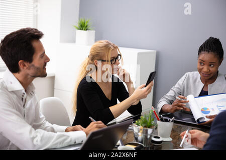 Young Businesswoman Using Smart Phone Sitting With Her Colleagues Discussing About Office Reports Stock Photo