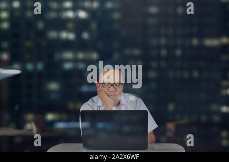 Young male student in school uniform wearing eye glasses falling asleep while doing his project and research in front of his laptop. Studying at night Stock Photo
