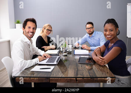 Group Of Smiling Business People Looking At Camera Sitting With Laptop At Office Stock Photo