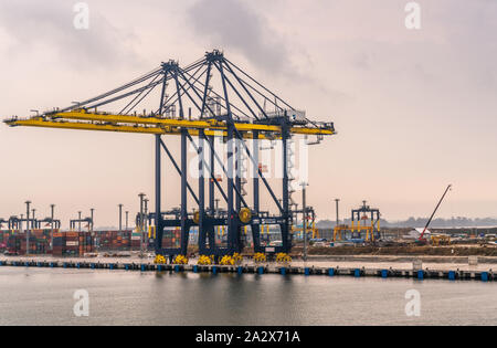 Laem Chabang, Thailand - March 16, 2019: Yellowand blue Cranes in Container port and terminal under gray cloudscape. Container stacks in back. Stock Photo