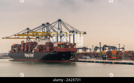 Laem Chabang, Thailand - March 16, 2019: Container port and terminal and Hapag Lloyd ship under gray sky. Yellow cranes loading and unloading it. Colo Stock Photo