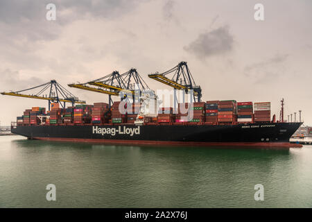 Laem Chabang, Thailand - March 16, 2019: Container port and terminal and Hapag Lloyd ship under gray sky. Four yellow cranes loading and unloading it. Stock Photo