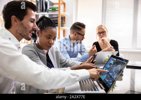 Side View Of Businesspeople Examining Graph On Computer At Workplace
