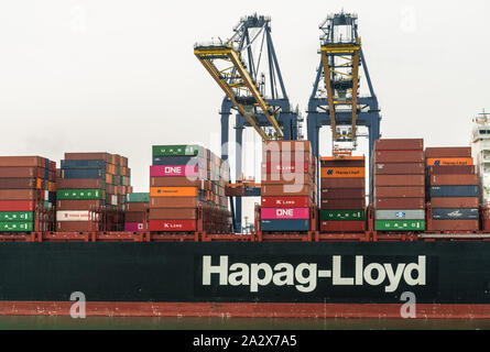 Laem Chabang, Thailand - March 16, 2019: Container port and terminal and mid section of Hapag Lloyd ship under gray sky. Two yellow cranes loading and Stock Photo