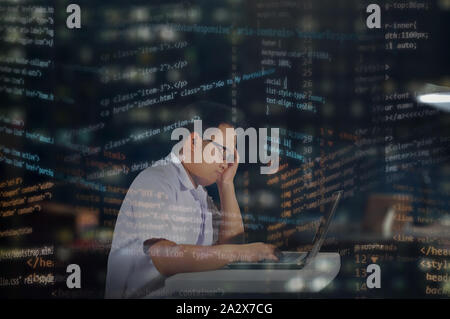 Young Asian male student in school uniform with glasses surrounded by overlay HTML codes, tired and sleepy after writing codes for website development Stock Photo