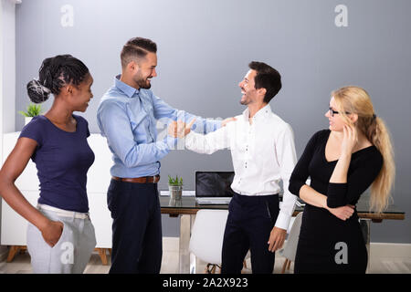 Women Looking At Happy Young Business Men Shaking Hands In Meeting Room Stock Photo