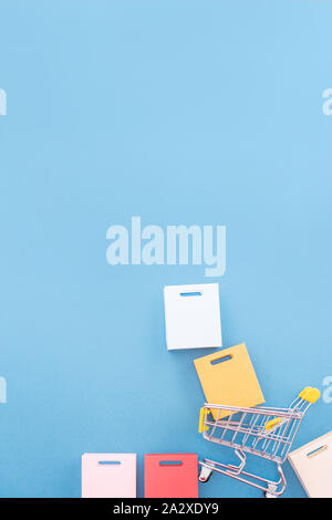 Abstract design element, annual sale, shopping season concept, mini yellow cart with colorful paper bag on pastel blue background, top view, flat lay Stock Photo