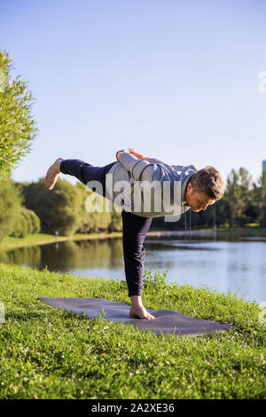 Inspired man doing yoga asanas in city park. Fitness outdoors and life balance concept. Stock Photo