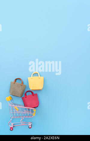 Abstract design element, annual sale, shopping season concept, mini yellow cart with colorful paper bag on pastel blue background, top view, flat lay Stock Photo