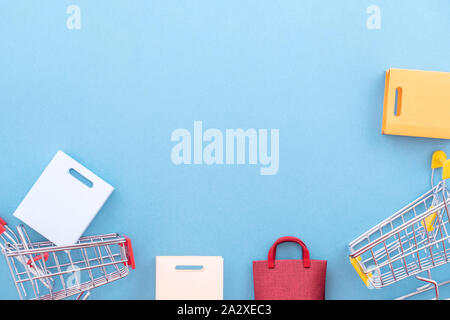 Abstract design element, annual sale, shopping season concept, mini yellow cart with colorful paper bag on pastel blue background, top view, flat lay Stock Photo