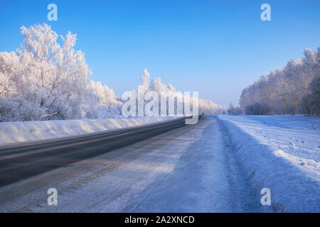 Siberian rural empty asphalt road under the snow. Siberian rural winter landscape with birch trees covered with hoarfrost on background Stock Photo