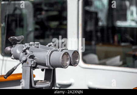 Repeatedly magnifying marine naval binoculars mounted on a bracket on the deck of a patrol ship provides the ability to monitor floating vessels in a Stock Photo