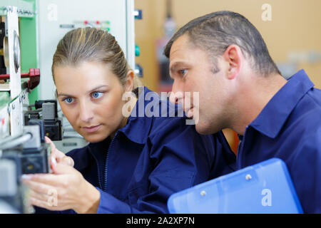 supervisor watching over female apprentice setting up machine Stock Photo