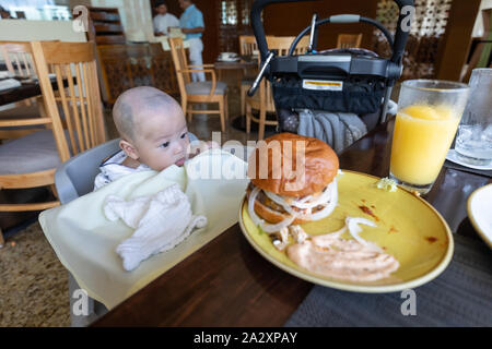 Happy baby sitting in high chair with hambuger at restaurant Stock Photo Alamy