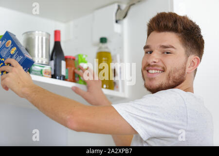 young man putting food away in the cupboard Stock Photo