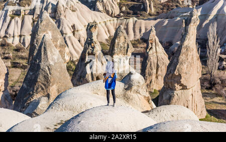 A Turkish woman wearing stripped hijab standing on the top of the sandrock, looking at the vocanic rocks in the park, Goreme, Cappadocia, Turkey. Stock Photo