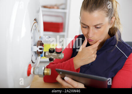 female technician servicing a boiler using tablet computer Stock Photo