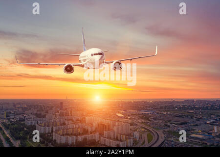 Panoramic view over the evening city during sunset, and a flying passenger plane Stock Photo