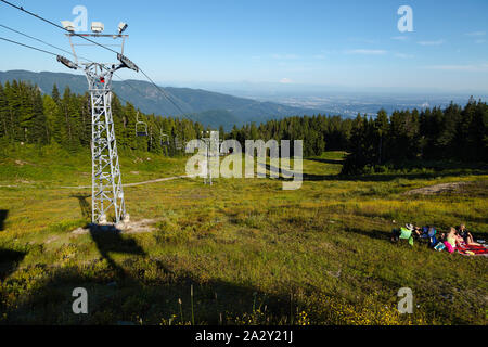 The ski lift next to the ski run hiking trail at the top of Seymour Mountain in North Vancouver, BC, with a view of the Fraser Valley and Mt. Baker in Stock Photo