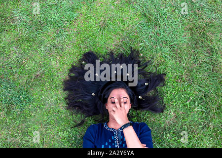 Beautiful young girl lying on grass with hair spread out covering her face with hand Stock Photo