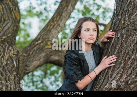 beautiful girl looking aside close to big tree trunk Stock Photo