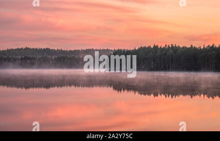 Beautiful sunrise landscape with misty mood and calm lake at foggy summer morning in Finland Stock Photo