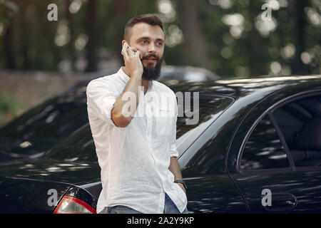 Handsome man in a white shirt. Businessman working with smartphone. Man standing near a car Stock Photo