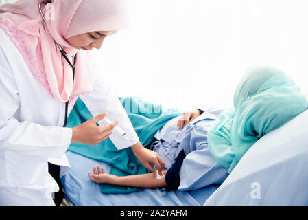 A beautiful young Muslim woman doctor wearing headphones, hand-held syringes, and a cotton ball is about to be injected into the arm of a sick patient Stock Photo