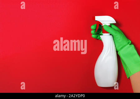 Worker's hand in a rubber green protective glove with a spray bottle on a red color background. The concept of cleaning, home care. Stock Photo